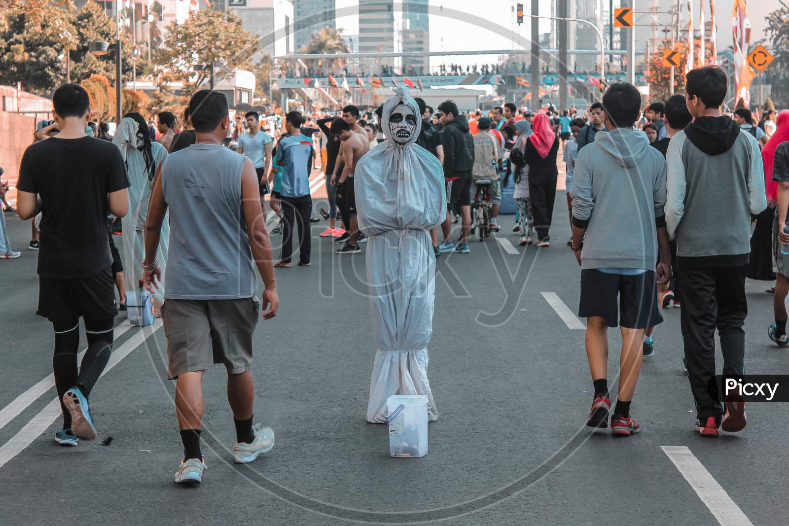  A person dressed in a traditional Indonesian pocong ghost costume walks down a busy street during a parade.