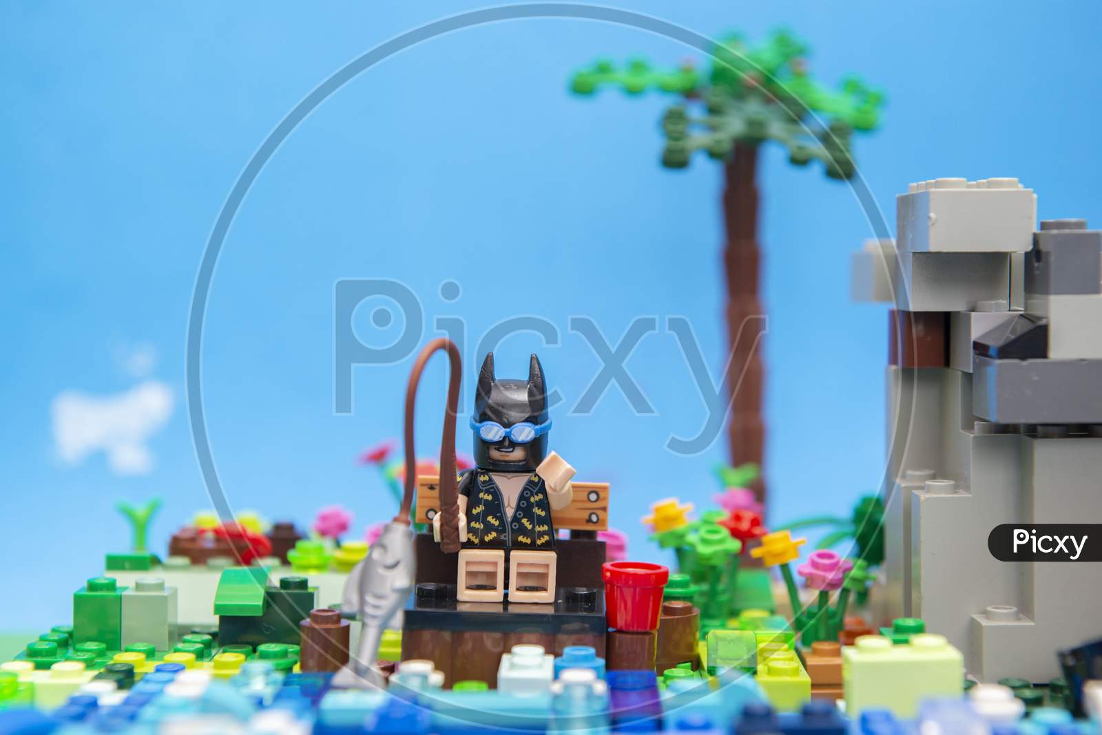 Florianopolis, Brazil. September 20, 2020: Batman Minifigure Sitting On A Wooden Bench Enjoying His Vacation And Fishing By The River Next To A Hillside. Concept Of Everyone Deserves Rest.