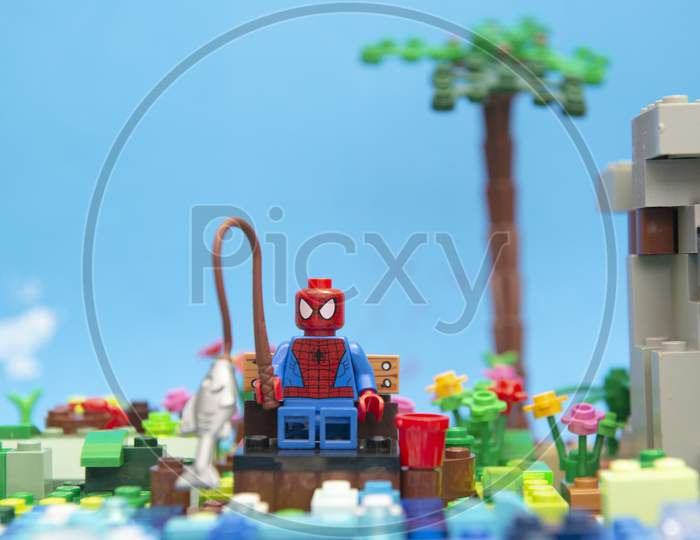 Florianopolis, Brazil. September 20, 2020: Spider Man Minifigure Sitting On A Wooden Bench Enjoying His Vacation And Fishing By The River Next To A Hillside. Concept Of Everyone Deserves Rest.