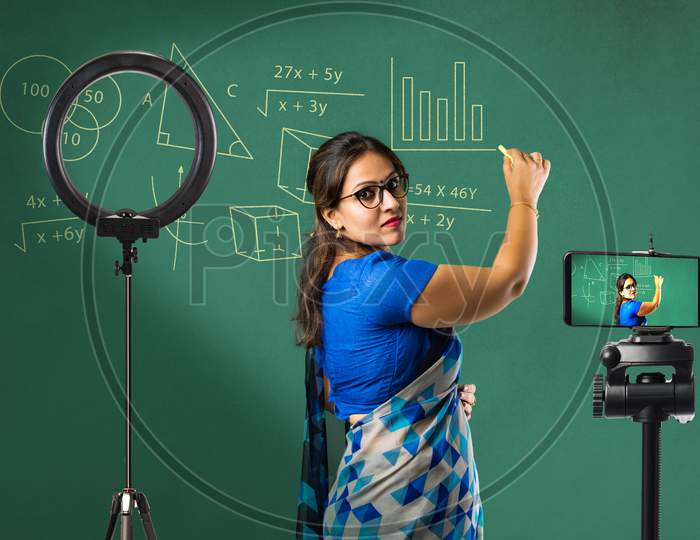 Portrait Of Asian Indian Lady Teacher In Saree Stands Against Writing Board Conducting Online Class