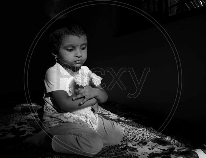 Indian Girl Child Holding Doll In W Shape Sitting Position In Low Key Light Monochrome Photo