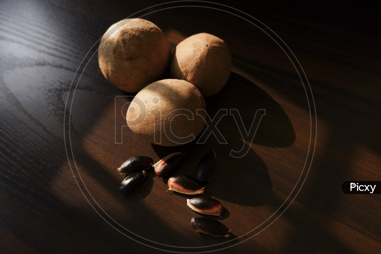 A Close Shot Of Sapota (Chikoo) Fruits & Seeds Isolated On Wooden Background