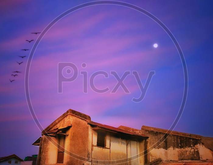Beautiful landscape of old village home with birds and moon in the sky at sunset time of monsoon with beautiful clouds