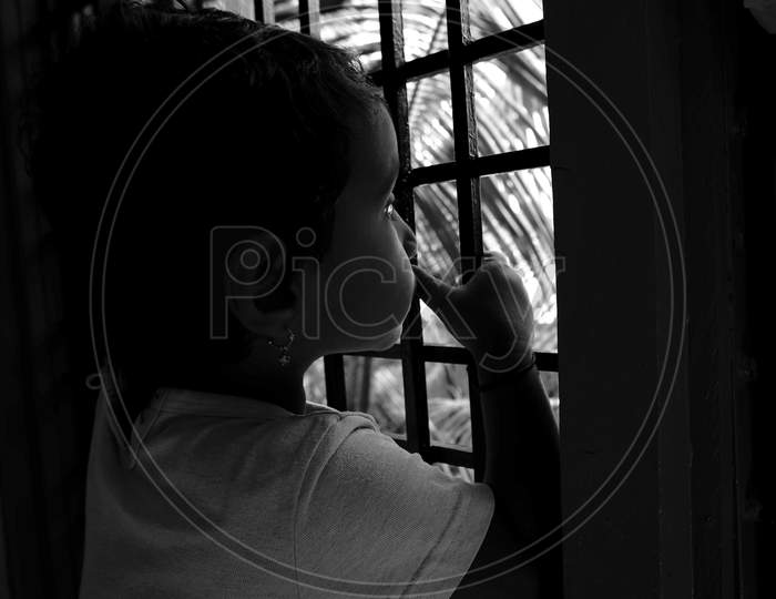 Close Shot Of Indian Girl Child Peeping In Window Outside The Nature In Monochrome Photo
