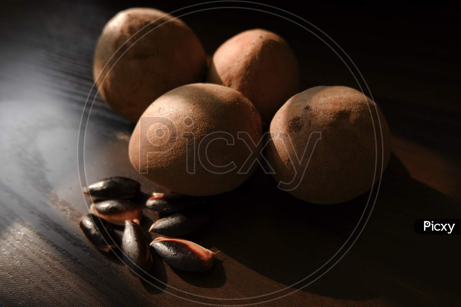 Close Shot Of Sapota (Chikoo) Fruits & Seeds Isolated On Brown Wood