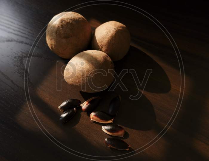 A Close Shot Of Sapota (Chikoo) Fruits & Seeds Isolated On Wooden Background