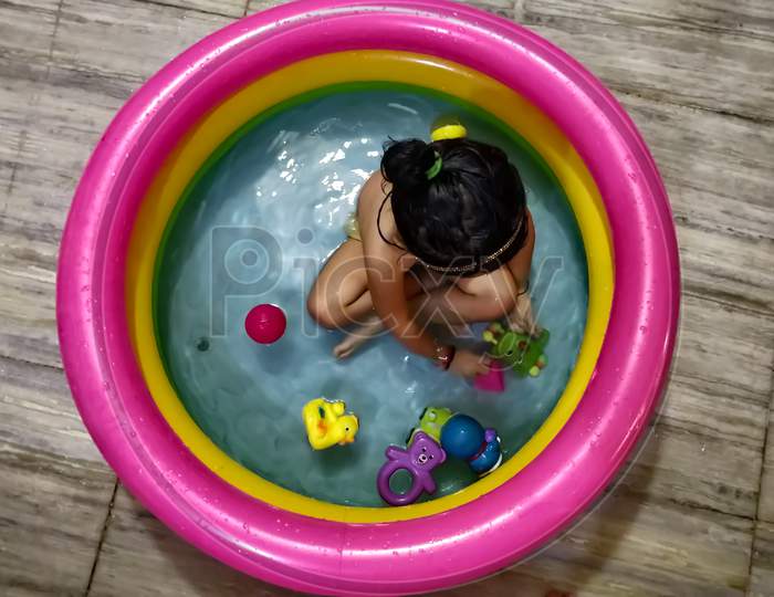 Happy Asian Indian little girl playing in the inflatable pool inside the house