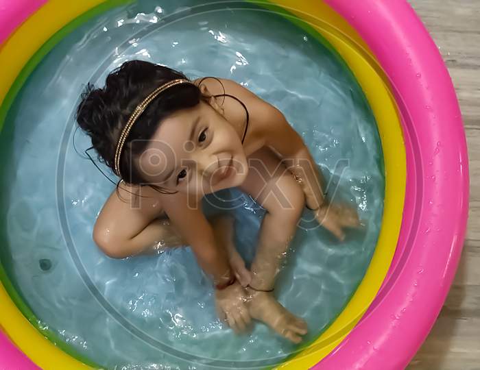 Happy Asian Indian little girl playing in the inflatable pool inside the house