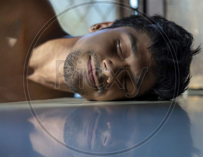 Peacefulness Concept. Creative Portrait Of A Young Man Lying On A Reflective Floor.