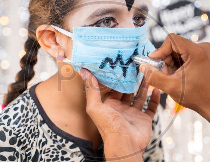 Kid Getting Ready Or Preparing For Halloween By Painting On Medical Face Mask - Concept Of Holiday, Halloween, And Childhood Festival Celebration And Preparation.