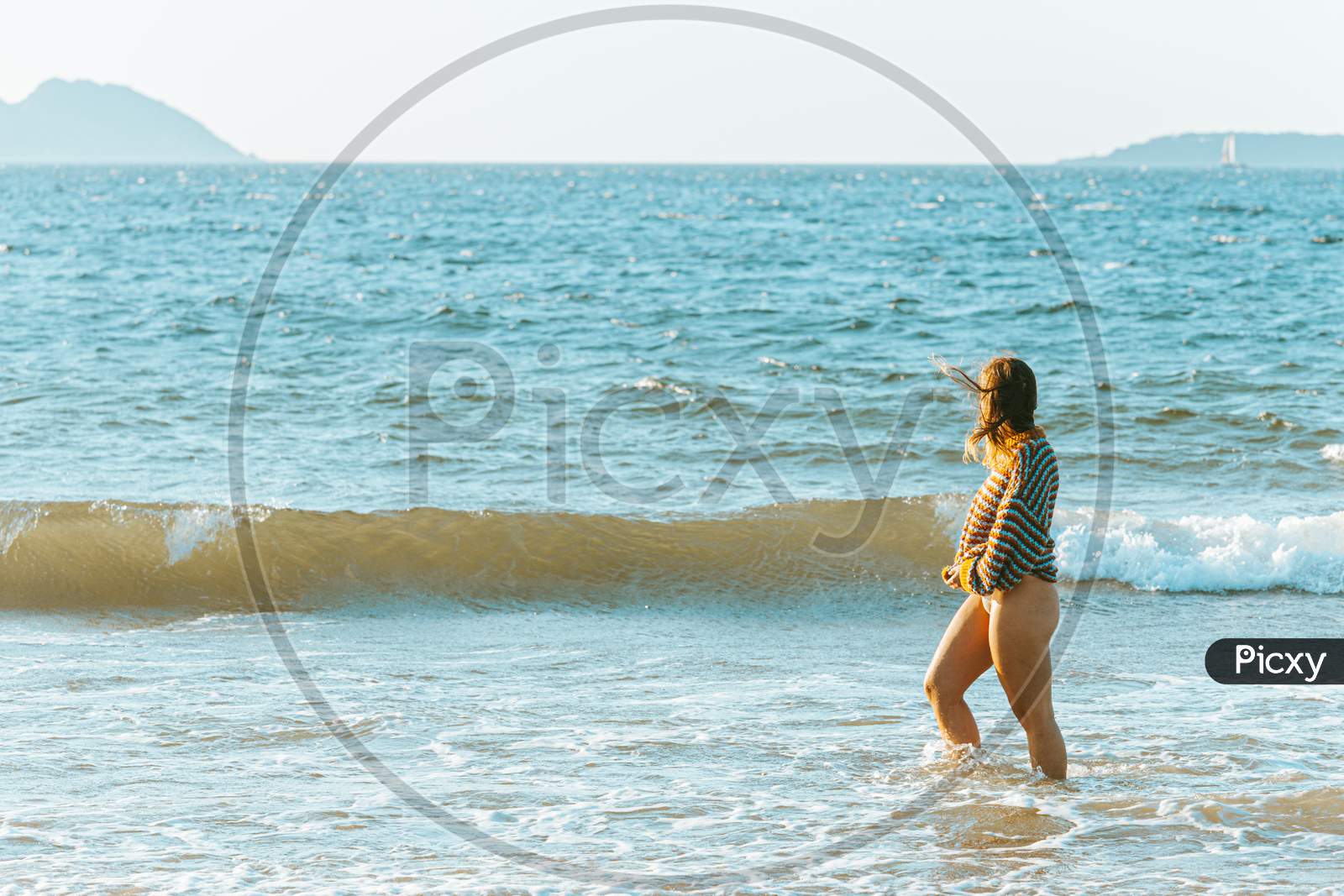 Young Woman Walking On The Sea In The Beach During A Bright Day With A Sweater Put On And Copy Space