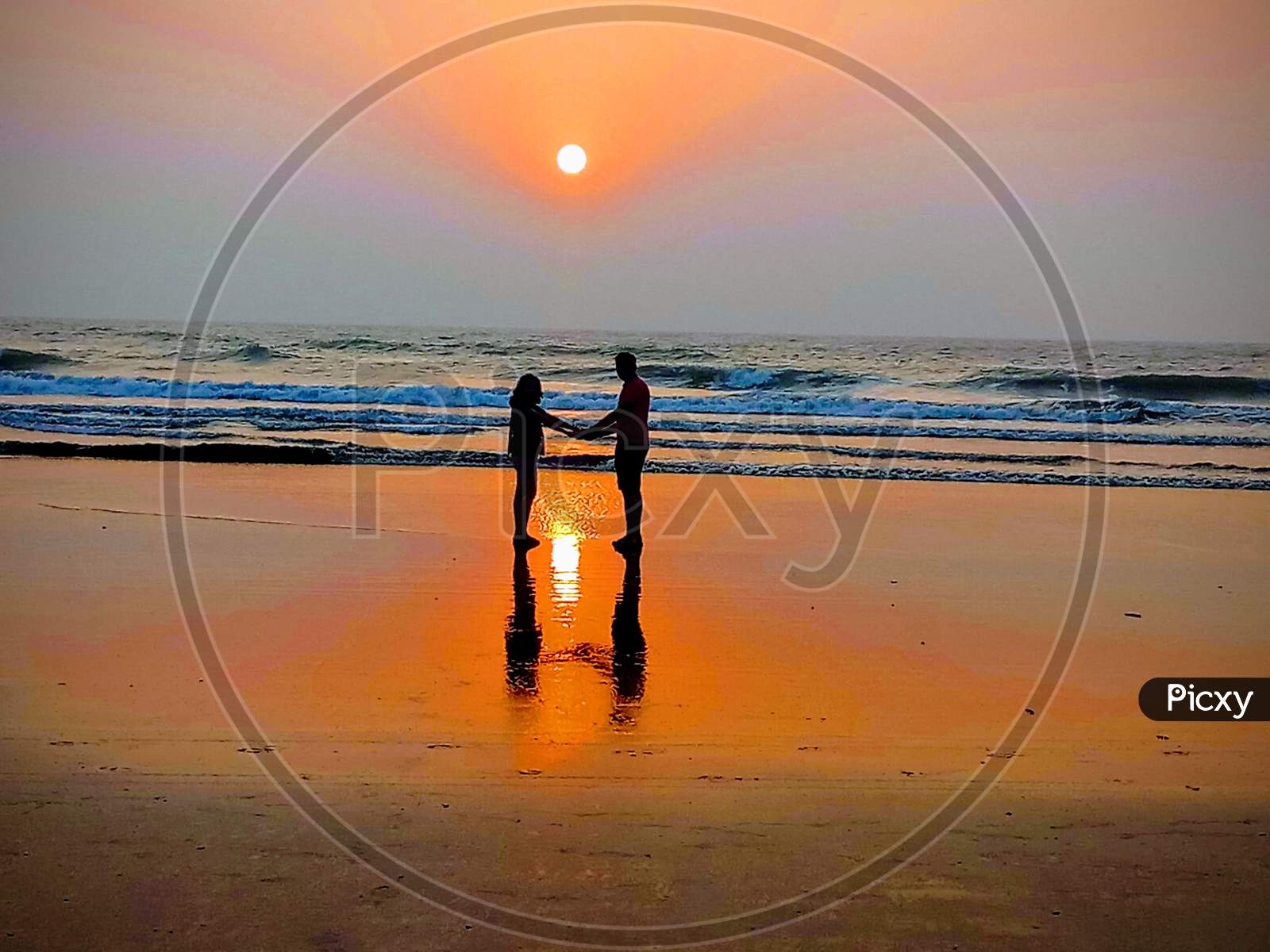 Sunrise at beach with couple holding hands and reflection on water with colorful scenery