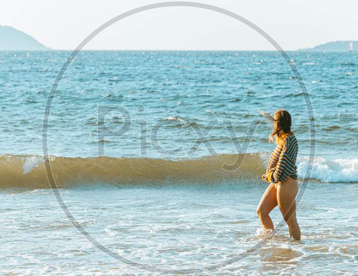 Young Woman Walking On The Sea In The Beach During A Bright Day With A Sweater Put On And Copy Space