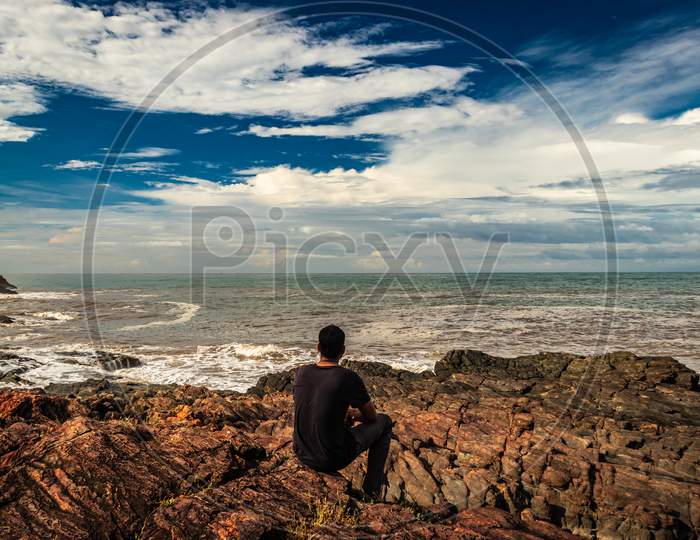 Man Sitting On Rock At Sea Shore In The Morning From Flat Angle