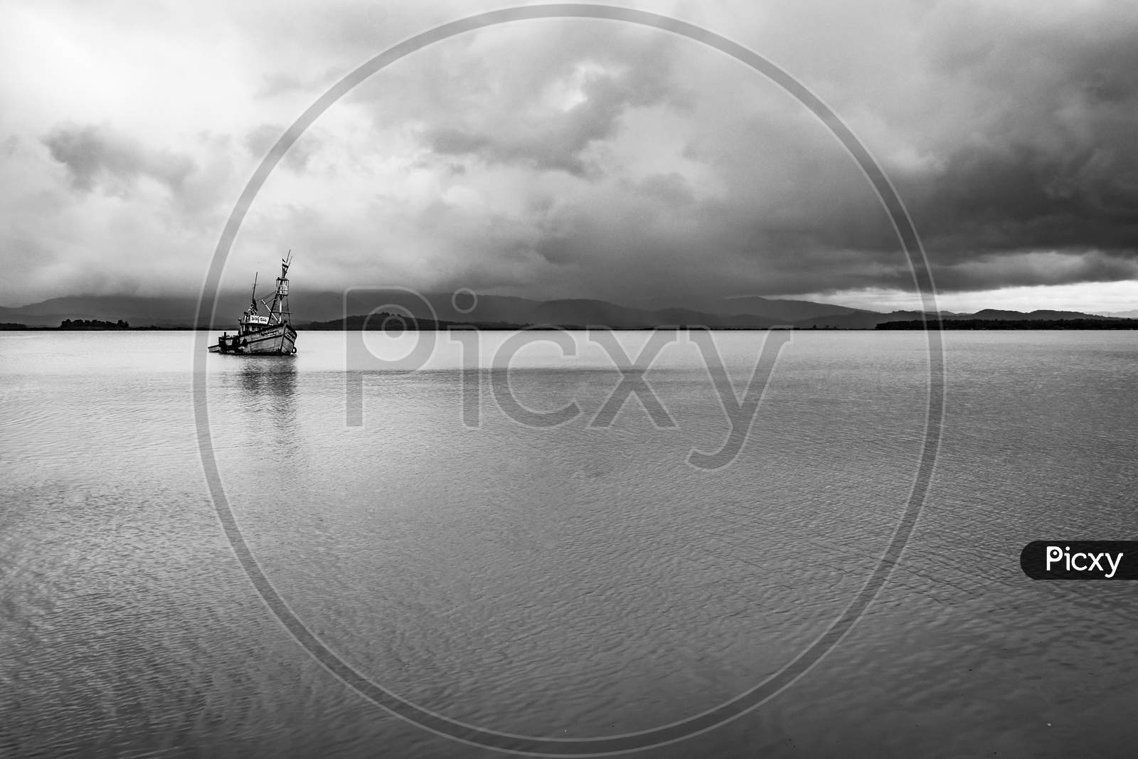 Fishing Boat Anchored At Sea Backwater With Dramatic Sky At Morning In Black And White