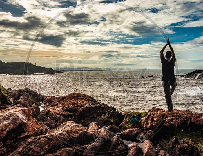 Man Doing Yoga Practice At Rock At Sea Shore At Morning From Flat Angle