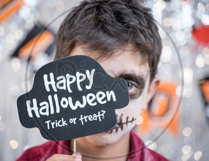 Kid Hloding Halloween Booth Prop Infront Of Spooky Face - Concept Of Halloween Trick Or Treat.