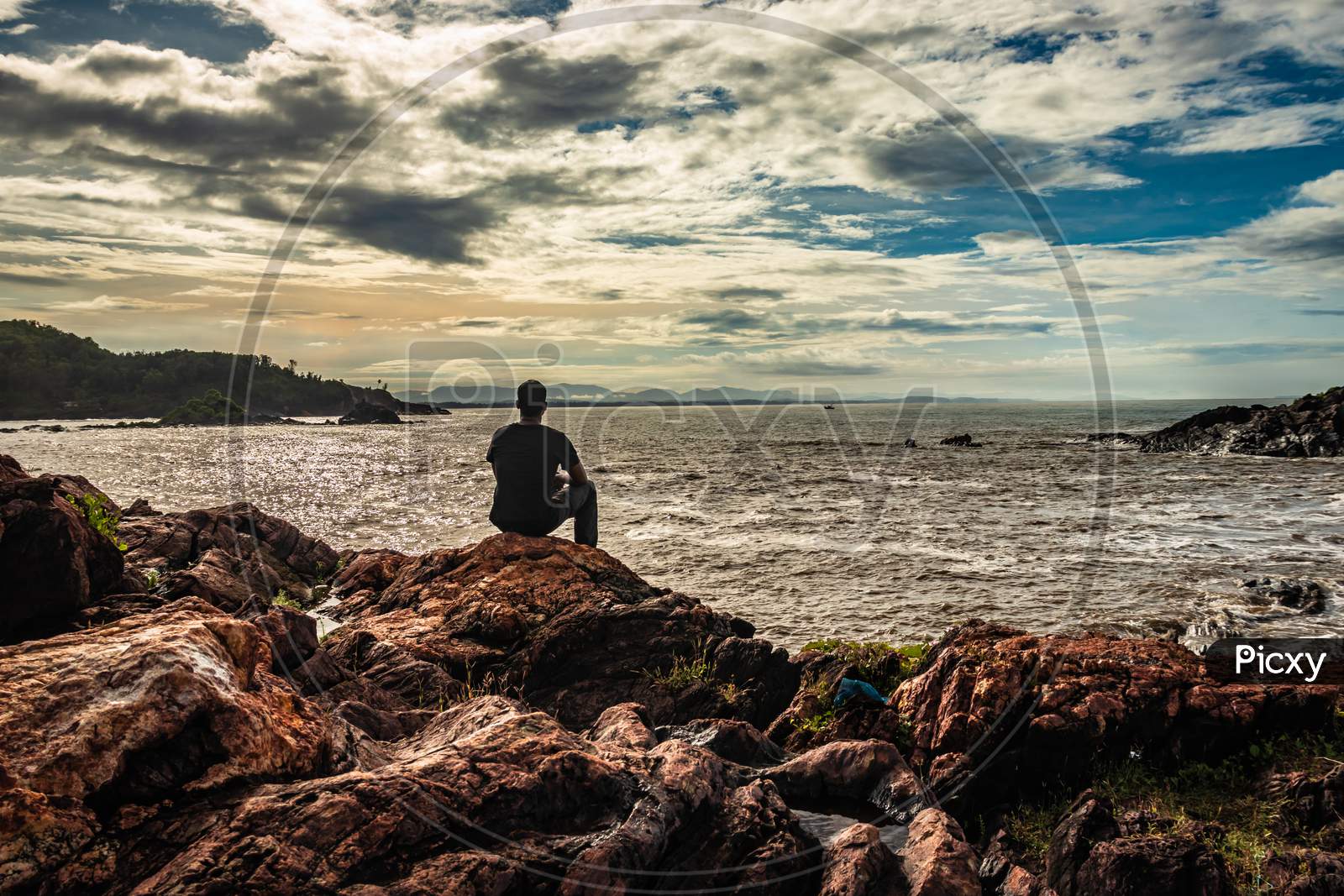 Man Sitting At Rock At Sea Shore At Morning From Flat Angle