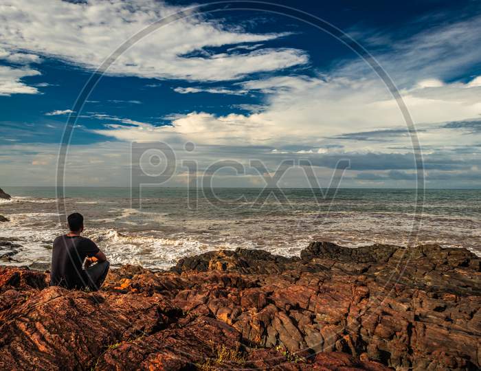 Man Sitting On Rock At Sea Shore In The Morning From Flat Angle