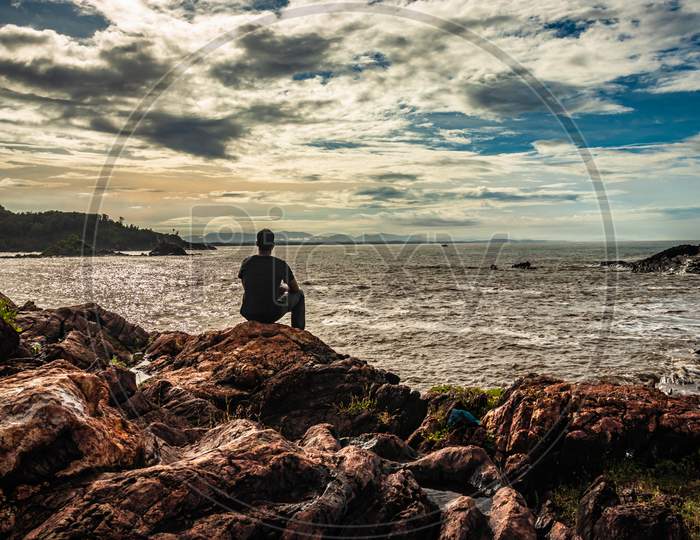 Man Sitting At Rock At Sea Shore At Morning From Flat Angle