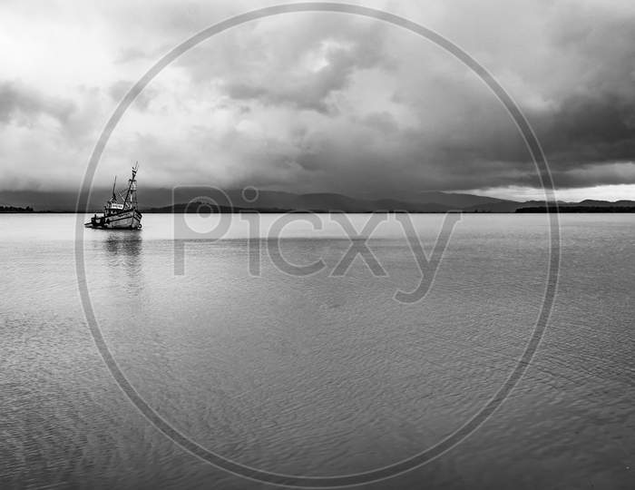Fishing Boat Anchored At Sea Backwater With Dramatic Sky At Morning In Black And White