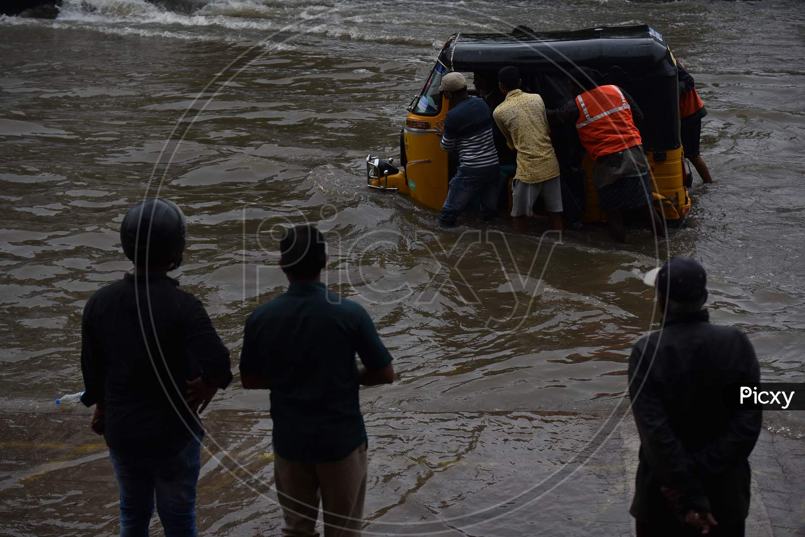 GHMC workers and passers by try to push an auto that got stuck in the rain water in Tolichowki,Hyderabad on October 14, 2020.