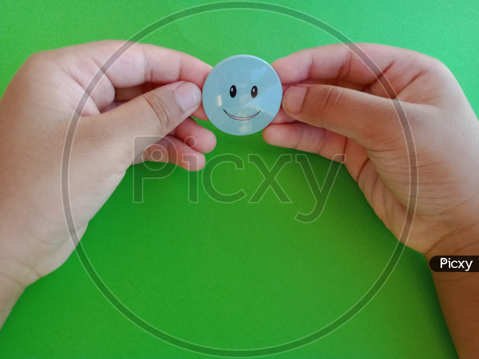 Small child's hand holding a smilie in green background