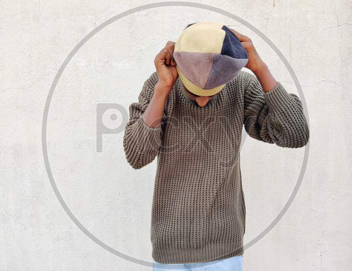 South Indian Young Man In Brown Sweater Is Trying To Wear Winter Hat . Isolated On White Background. Winter Portrait
