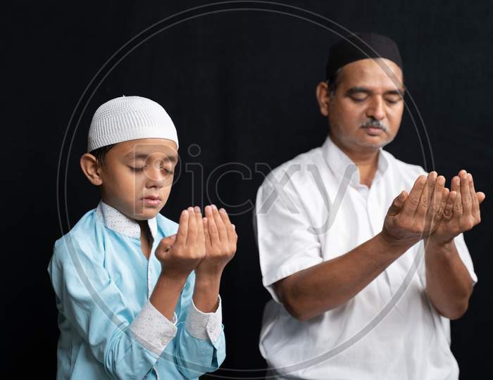 Muslim Father And Son In Medical Mask Praying Or Performing Salah O Protect From Coronavirus Or Covid-19 By Sitting.