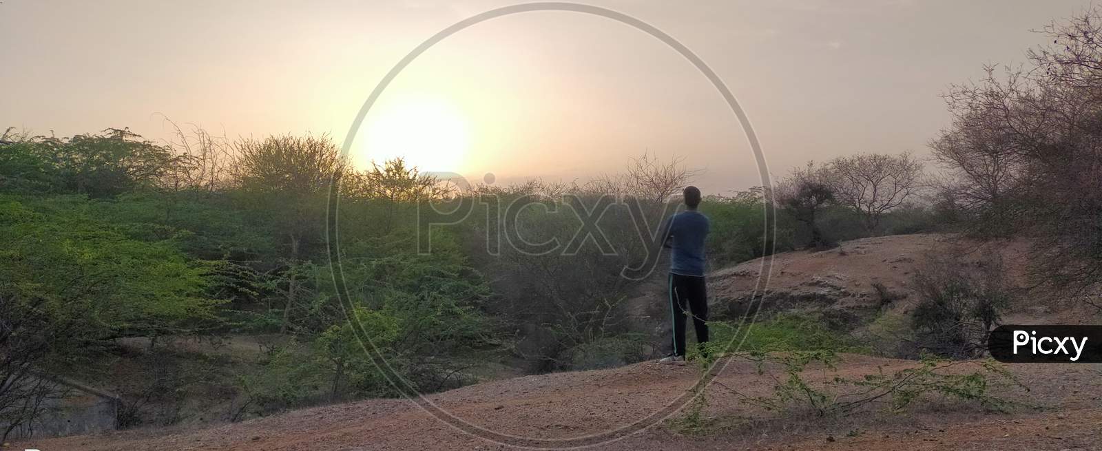 Man /Boy facing the Sunset in Aravali hills in forest