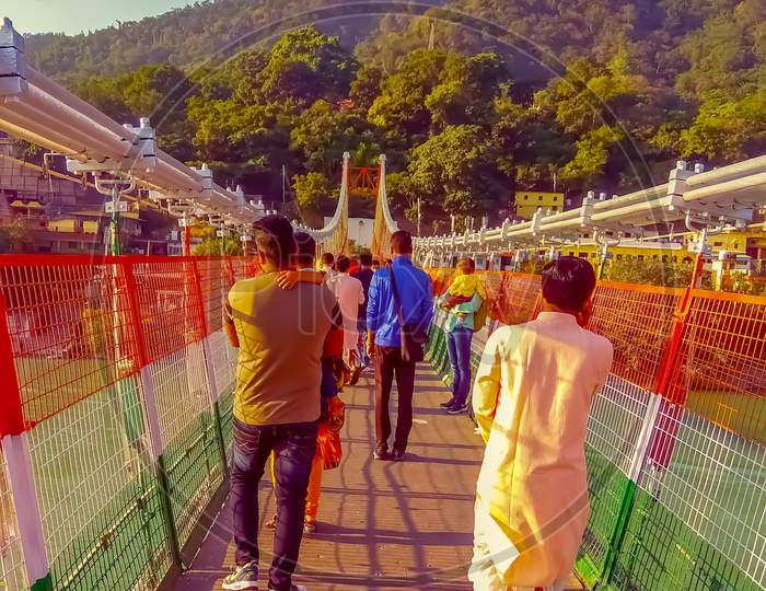 An Indian father holding his son and some tourist/people waking across Ram jhula bridge in Rishikesh, uttara khan.latest pic 2021