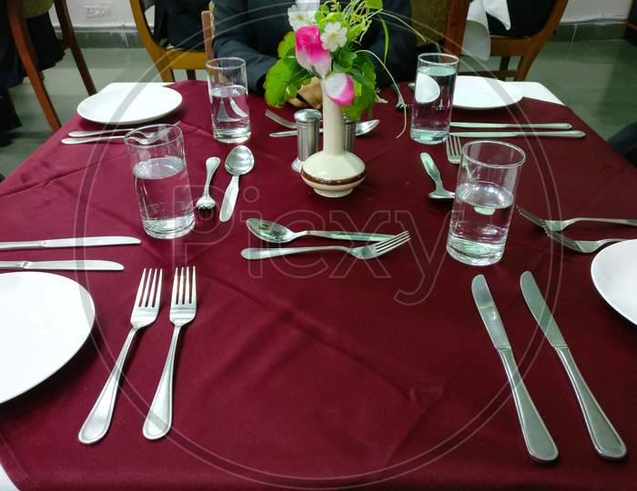 Table setting for elegant dinner with white plates, glasses, cutlery & flower pot.