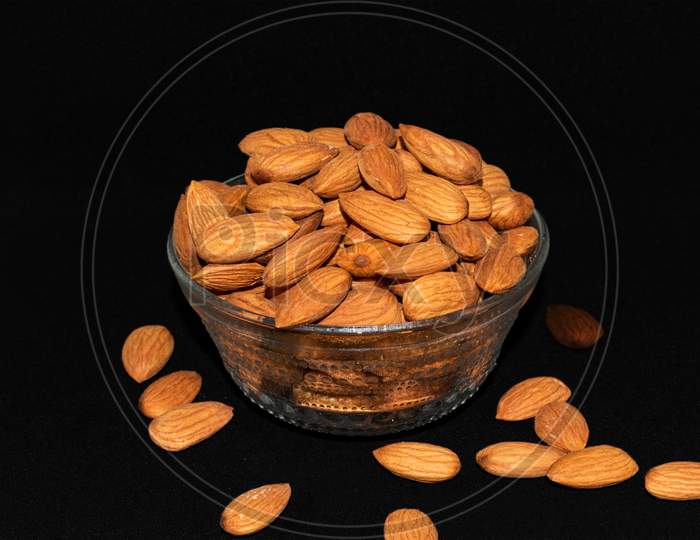 Glass bowl full of almond nuts isolated on dark rough background