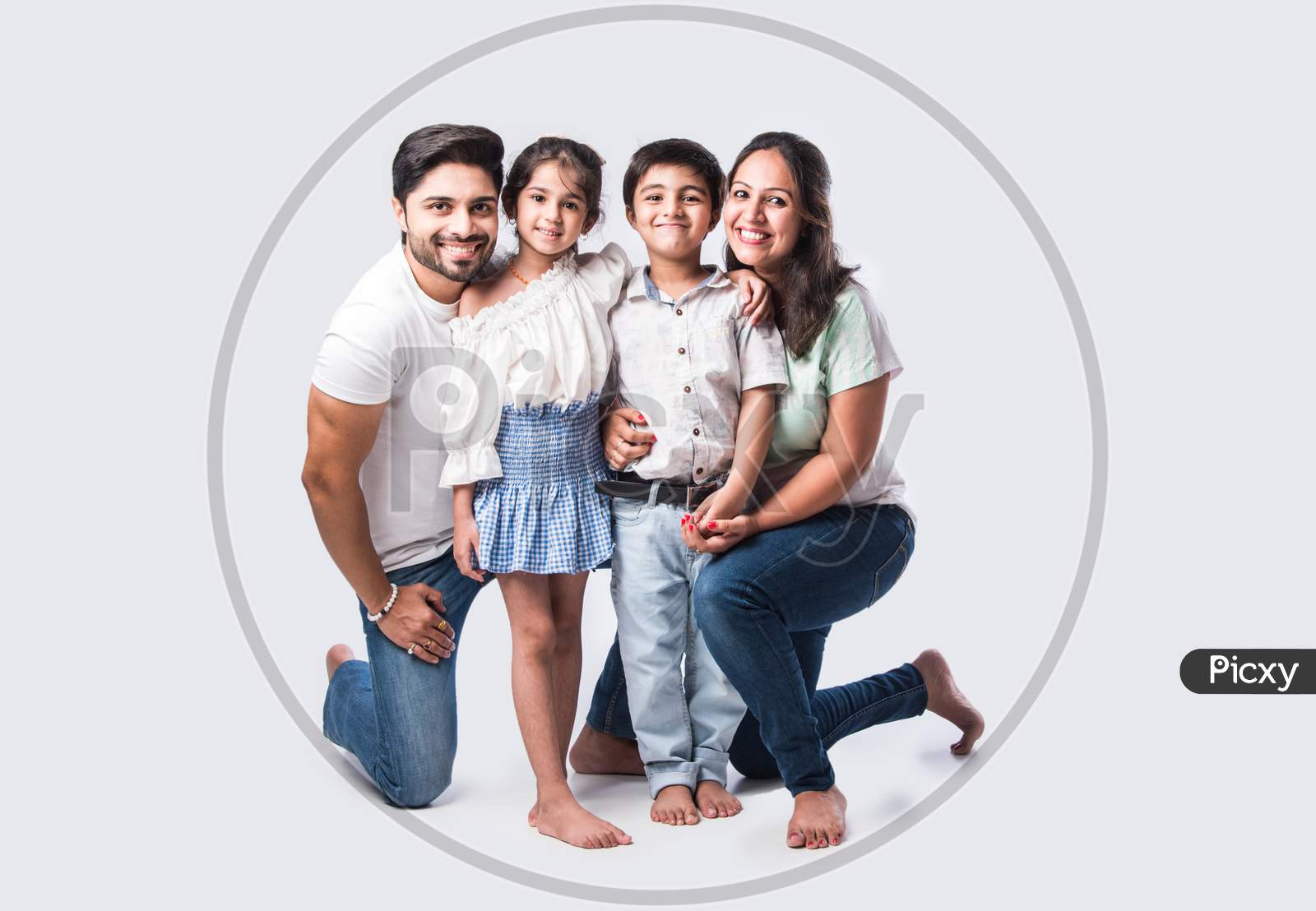 Beautiful Indian Young Family Of Four Hugging While Standing Against White Background