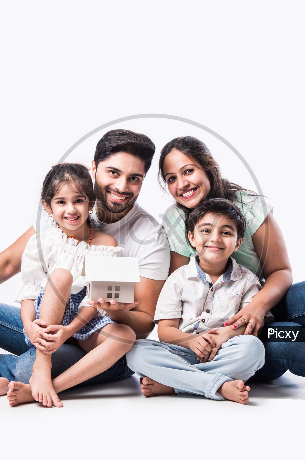 Real Estate Concept - Indian Happy And Young Family Of Four Holding 3D Paper Model Of Home