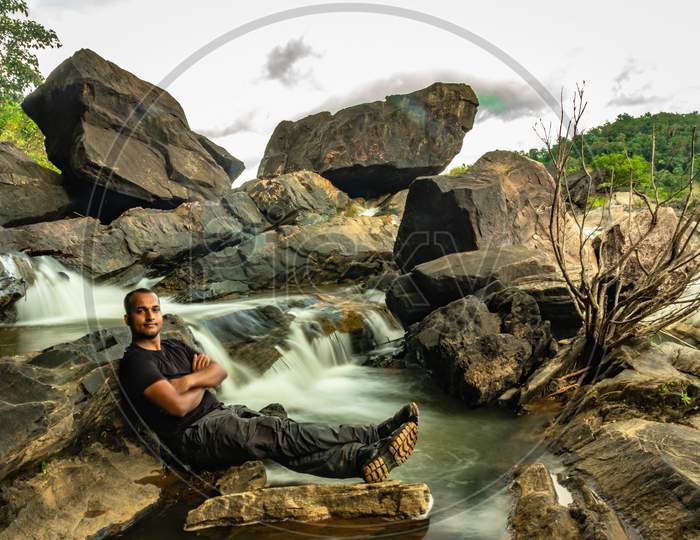 Man Relaxing At Rock With The Beautiful Waterfall Stream Long Exposure Shot At Evening