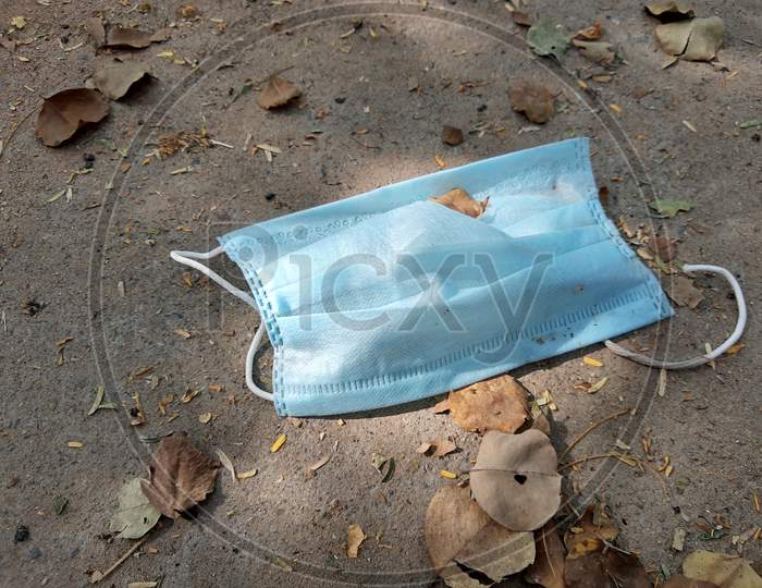Used Disposable Medical Blue Face Mask Discarded On The Ground Of A City Road Lane. Environmental Pollution And Waste During The Covid-19 ( Coronavirus ) Pandemic.