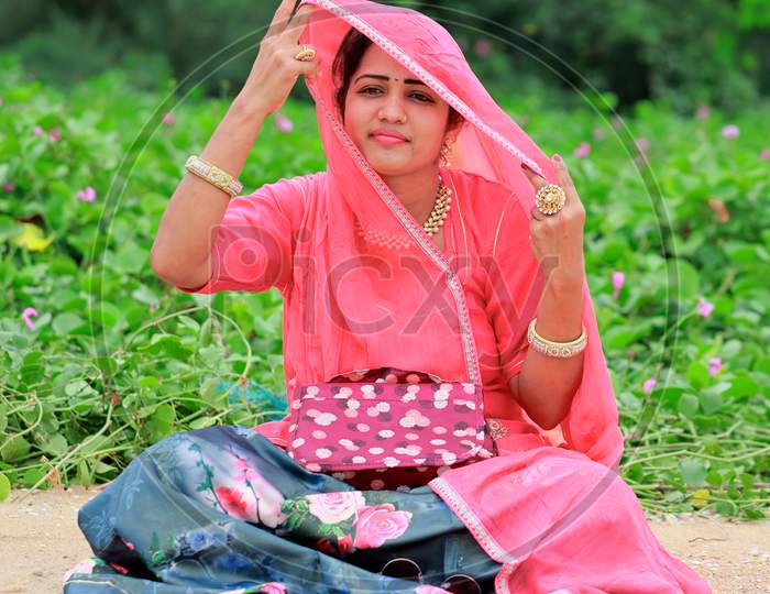 Young Indian Woman Sitting In The Garden, Lifting The Veil With Her Hand And Looking Away With A Smiling Face
