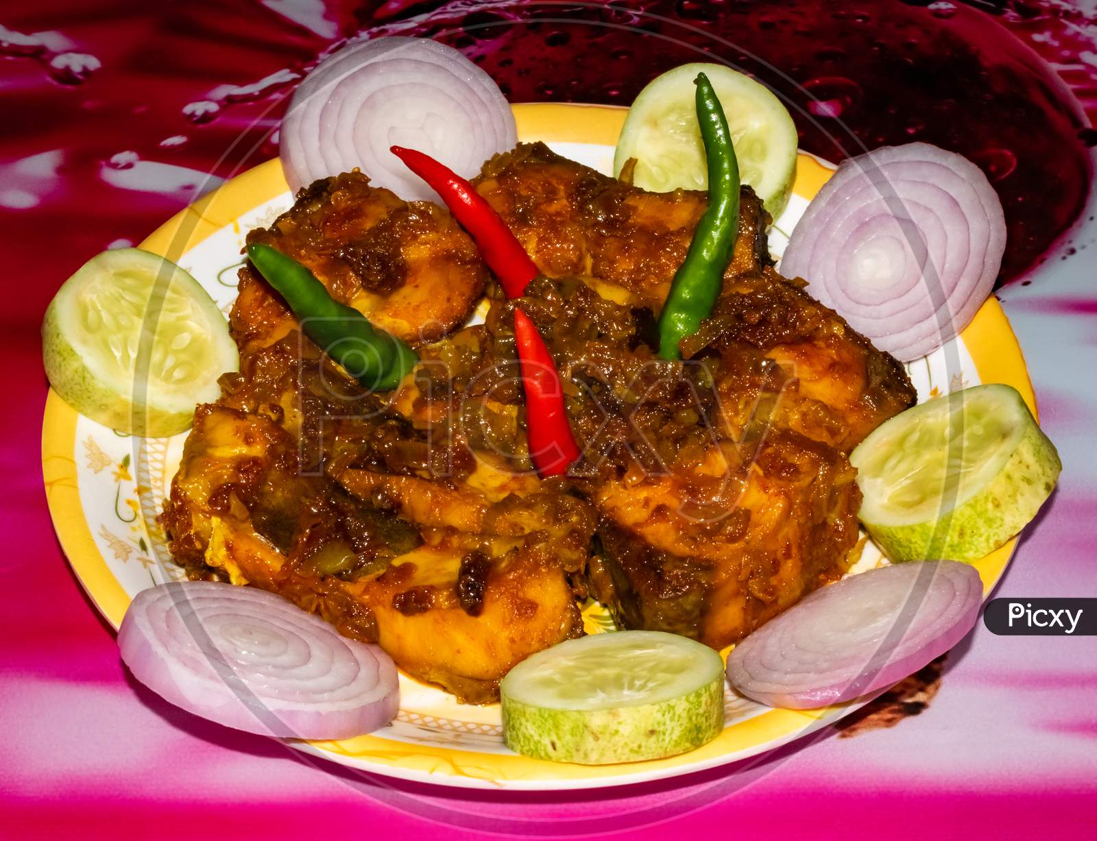 Spicy tasty Indian fish dish garnished with chili onion rings and cucumbers