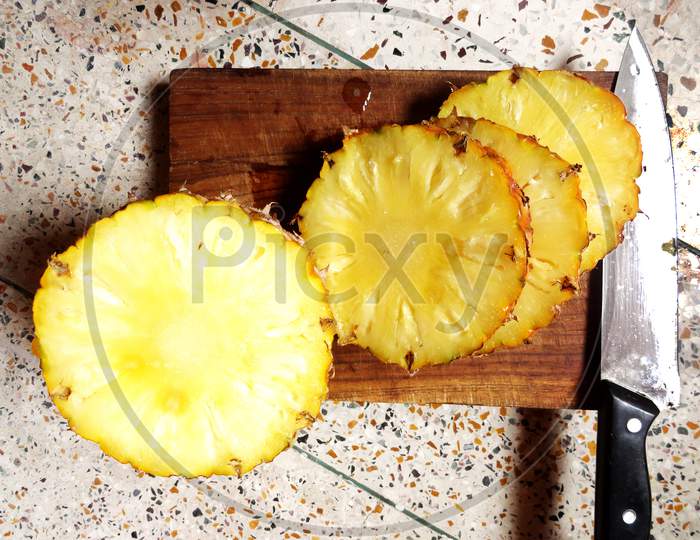 Sliced pineapple on a chopping board with a knife