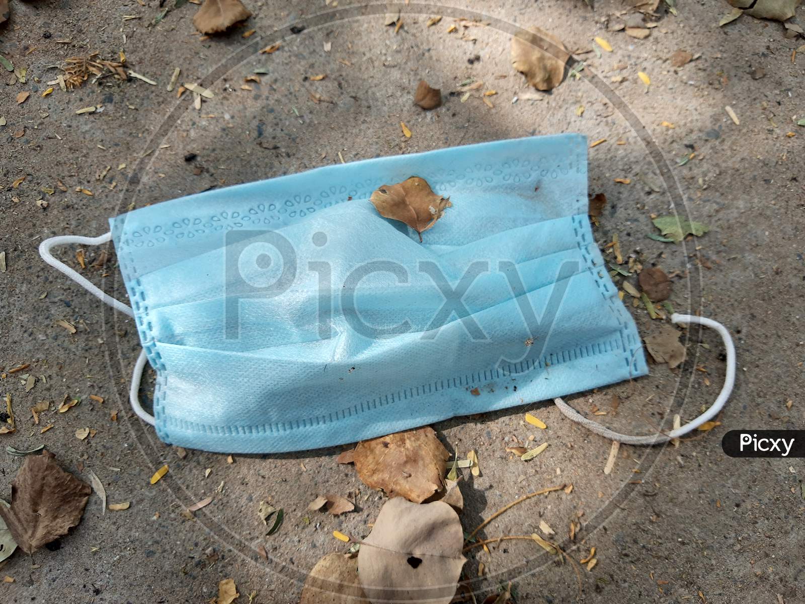 Used Disposable Medical Blue Face Mask Discarded On The Ground Of A City Road Lane. Environmental Pollution And Waste During The Covid-19 ( Coronavirus ) Pandemic.