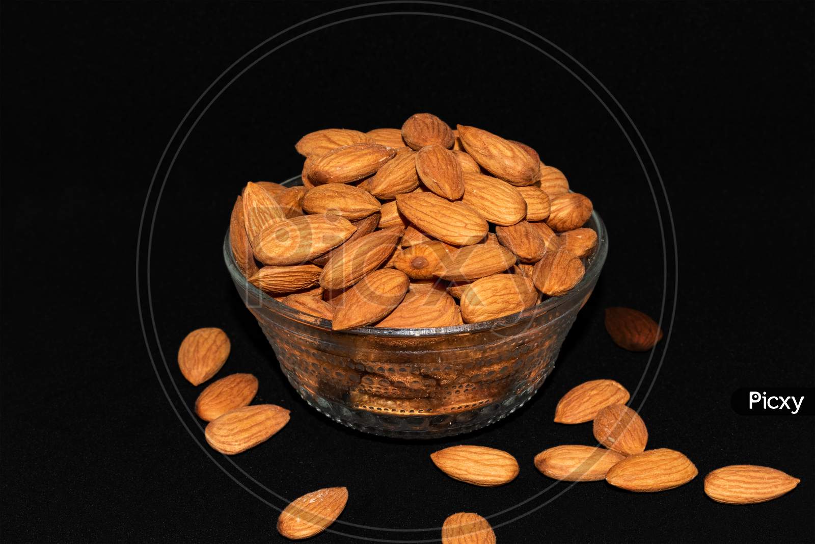 Glass bowl full of almond nuts isolated on dark rough background