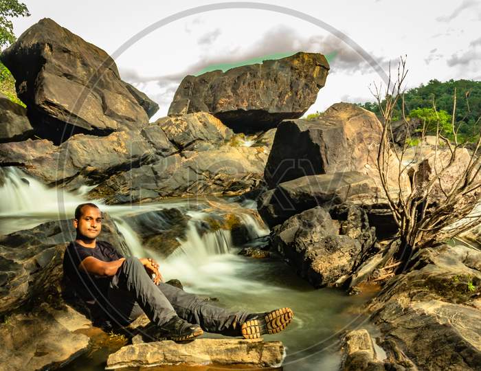 Man Relaxing At Rock With The Beautiful Waterfall Stream Long Exposure Shot At Evening