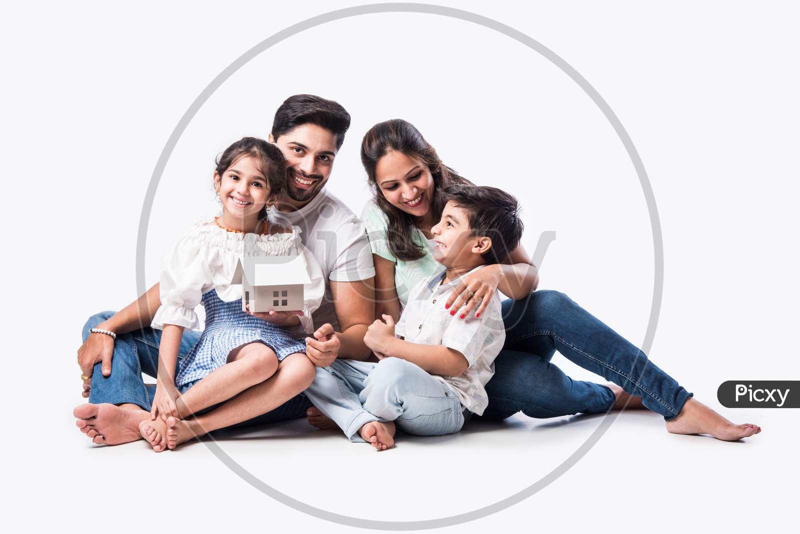 Real Estate Concept - Indian Happy And Young Family Of Four Holding 3D Paper Model Of Home
