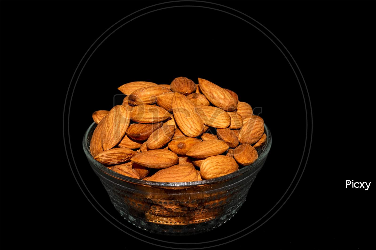 Glass bowl full of healthy fresh almond nuts isolated on black background