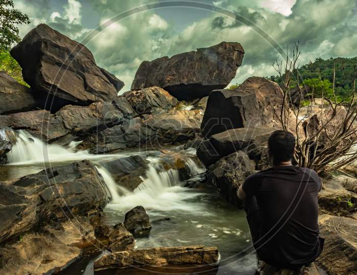 Man Sitting At Rock Watching The Beautiful Waterfall Stream Long Exposure Shot At Evening