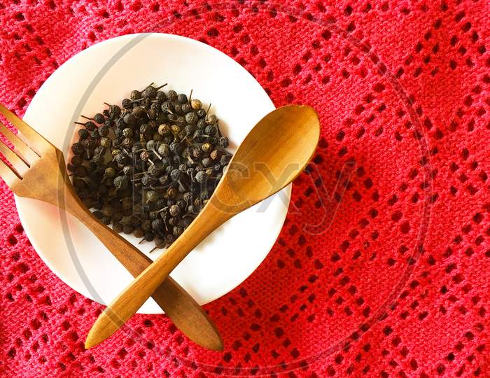 Collection of cubeb on a white plate with a spoon and a fork.