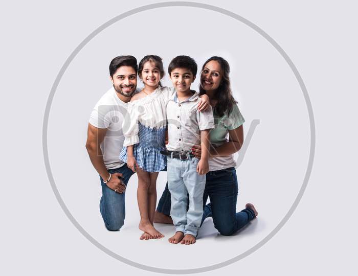 Beautiful Indian Young Family Of Four Hugging While Standing Against White Background