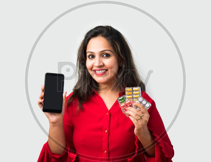 Indian Asian Young Woman Holding Medicines In Her Hand With Mobile App Screen