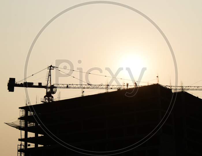 Silhouette Two engineers consult and inspect high-rise construction work over blurred industry background with Light fair on under construction building at sunset time with tower crane